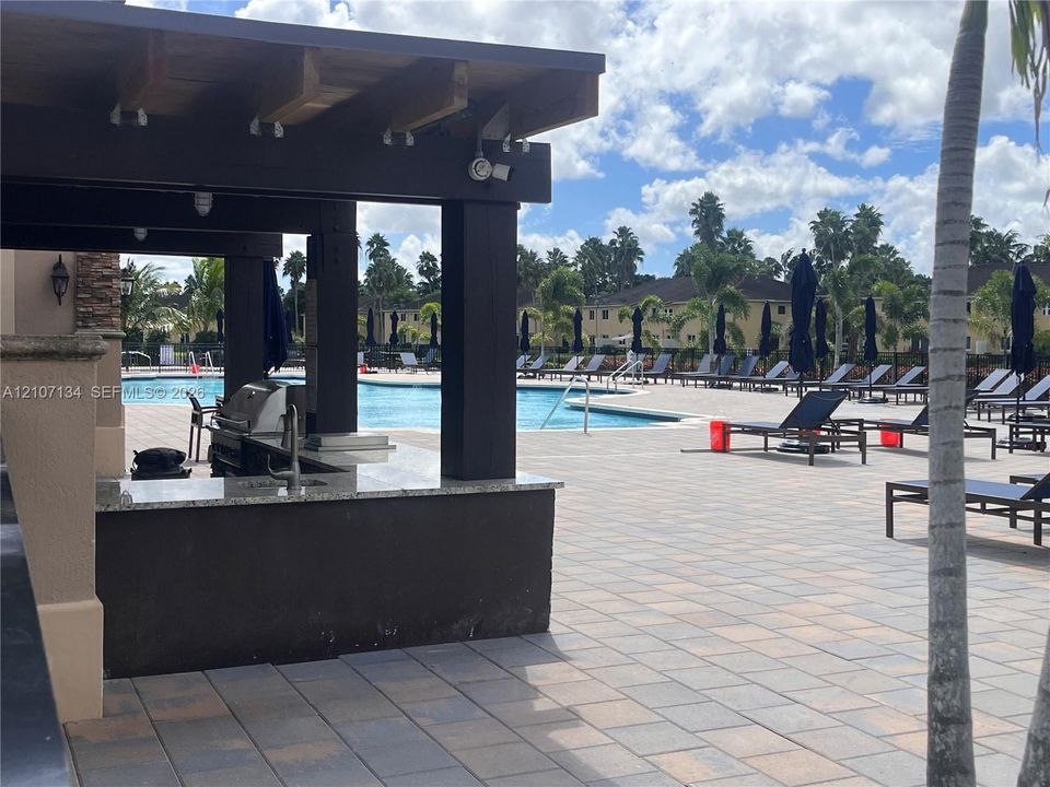 Outdoor kitchen area featuring a covered pergola, stone-finish countertops, and an integrated grill, complemented by an extensive paver patio surrounding a swimming pool