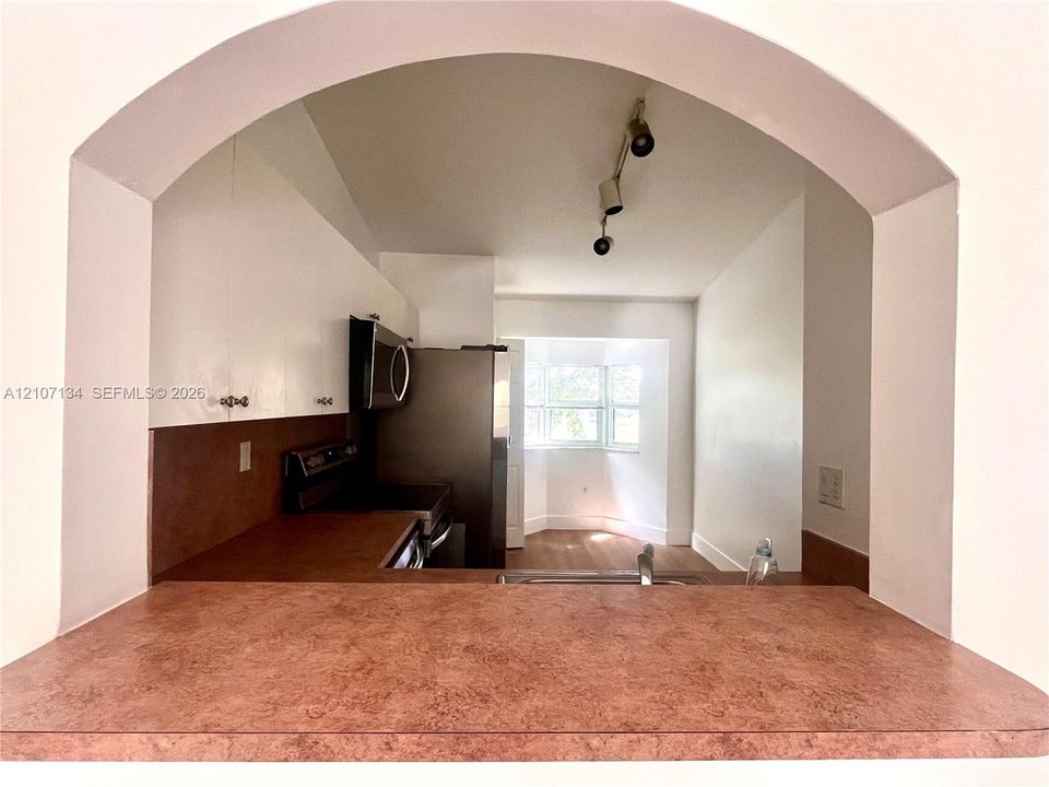 Arched pass-through featuring a textured countertop, white cabinetry, stainless steel appliances, track lighting, and wood-finish flooring