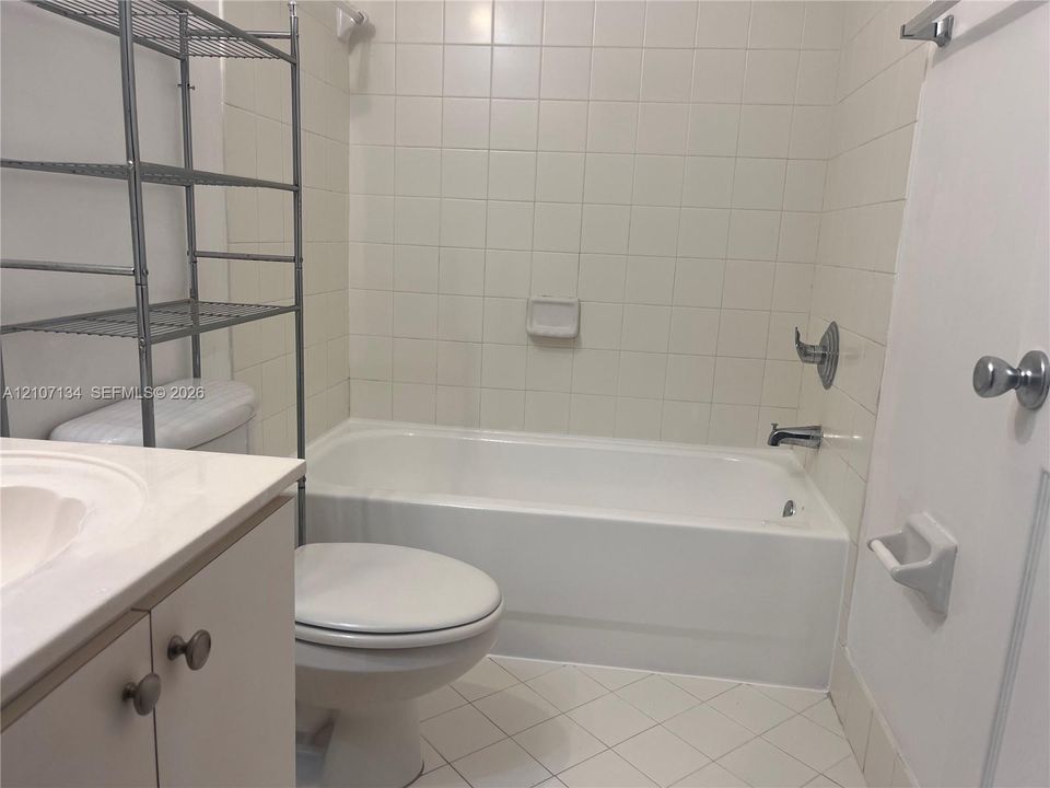 Bathroom featuring a white vanity with a composite countertop, an integrated sink, a porcelain soaking tub with tile surround, and diamond-pattern floor tiling