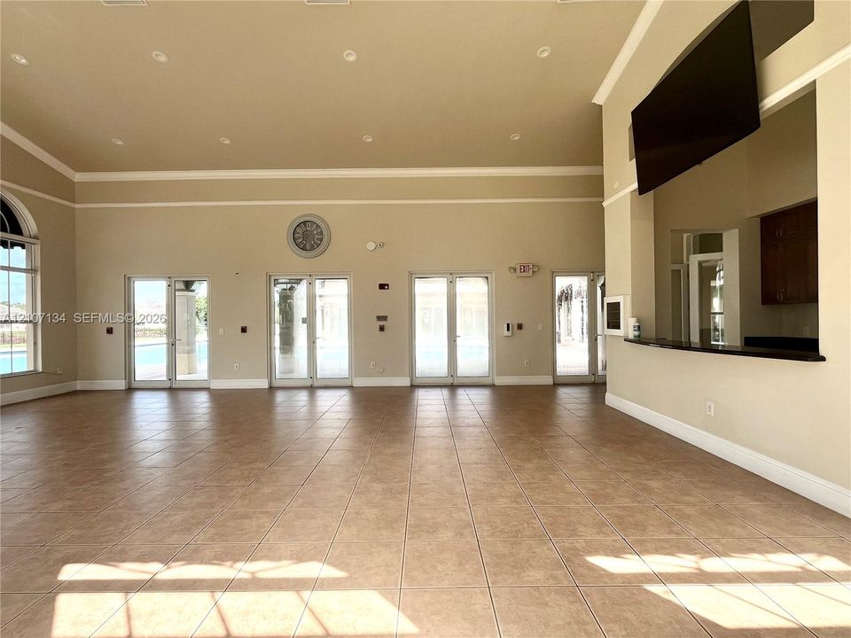 Expansive interior space featuring high ceilings, neutral ceramic tile flooring, recessed lighting, multiple sets of glass-paned double doors, and a built-in serving bar with a dark countertop