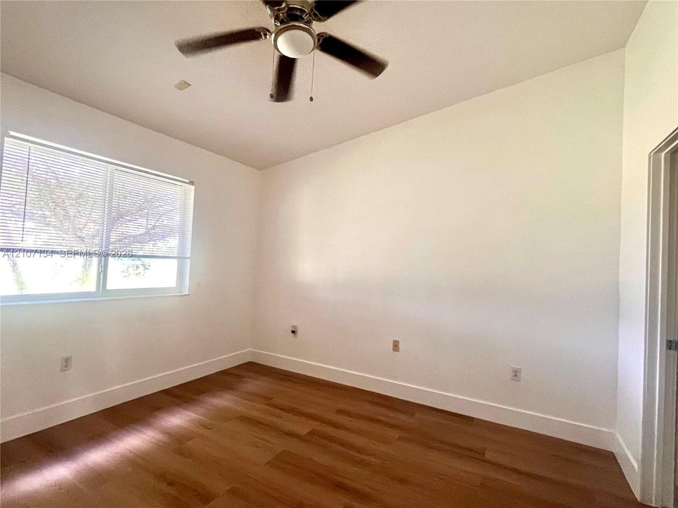 Neutral-toned room featuring wood-finish flooring, a ceiling fan with integrated lighting, and a large horizontal window