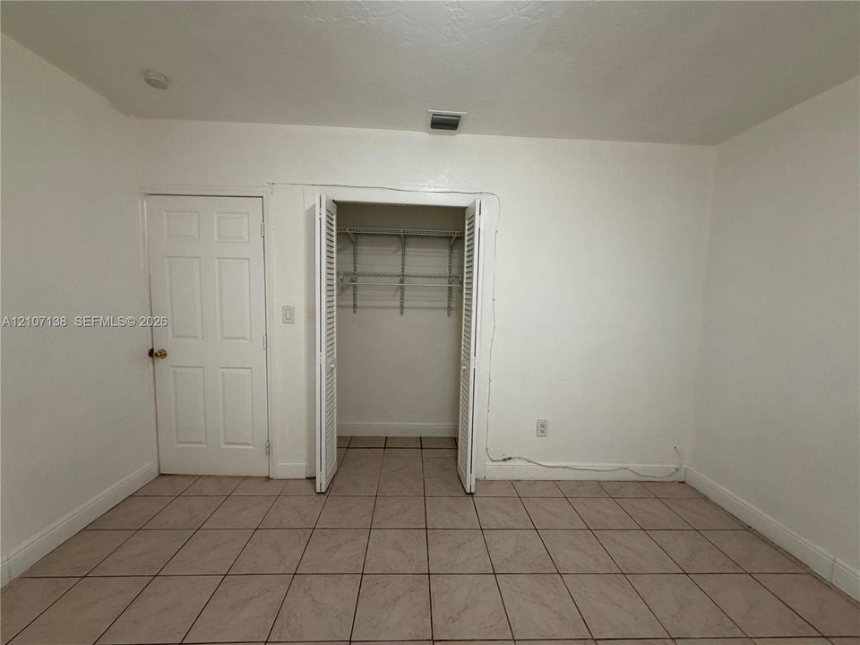 Square-tiled flooring, interior door with brass-finish hardware, and reach-in closet featuring bi-fold louvered doors and wire shelving