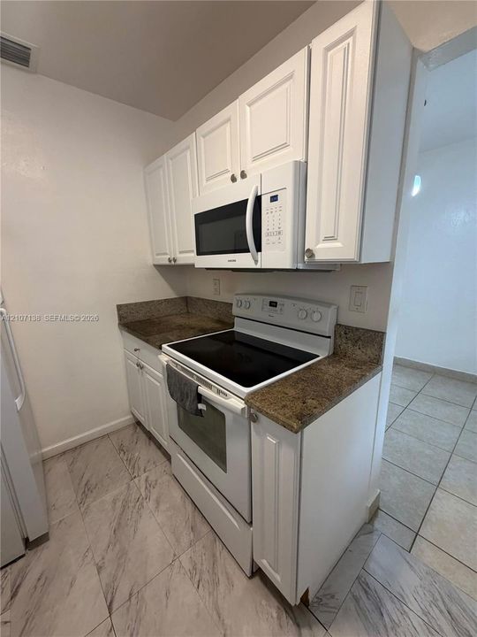 Kitchen featuring white shaker-style cabinetry, stone-finish countertops, built-in microwave, freestanding electric range, and tile flooring