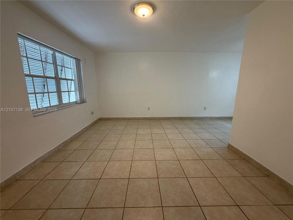 Neutral interior featuring light-toned floor tiling, smooth wall finishes, a single-pane window, and a flush-mount ceiling light fixture