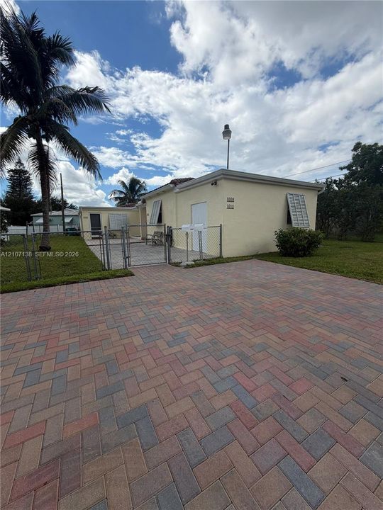 Exterior featuring a paved herringbone driveway, stucco siding, metal hurricane shutters, and a gated perimeter fence