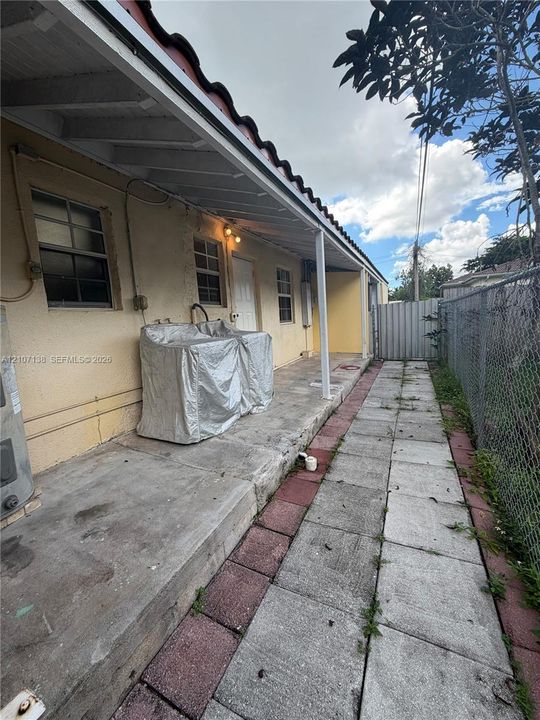 Covered exterior patio featuring a concrete foundation, tiled walkway, and chain-link perimeter fencing