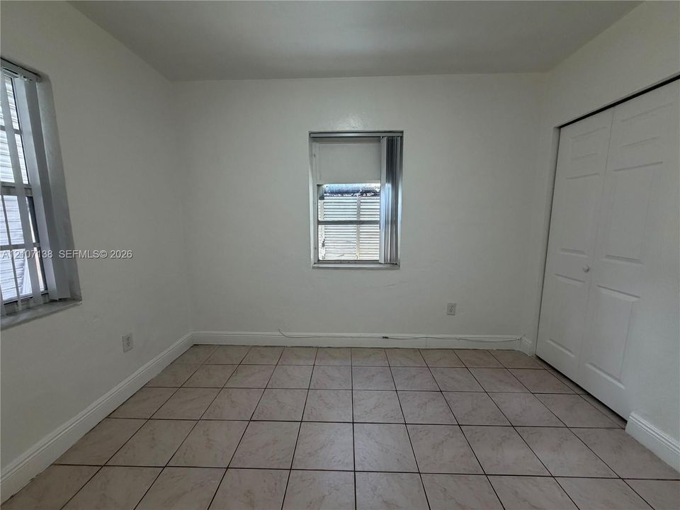 Interior room featuring neutral-toned floor tiling, dual windows with grid-pattern frames, and a white dual-panel closet door