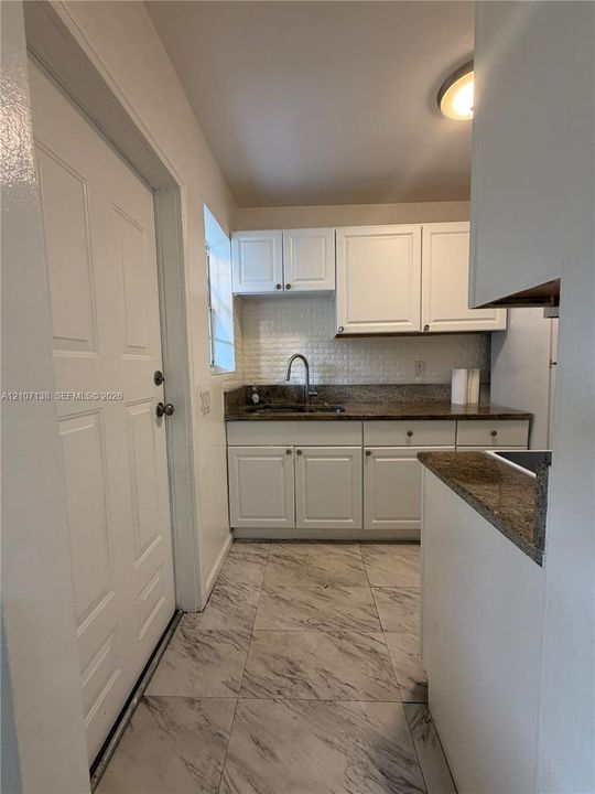 Kitchen featuring white Shaker-style cabinetry, stone-finish countertops, tiled backsplash, and stone-finish floor tile