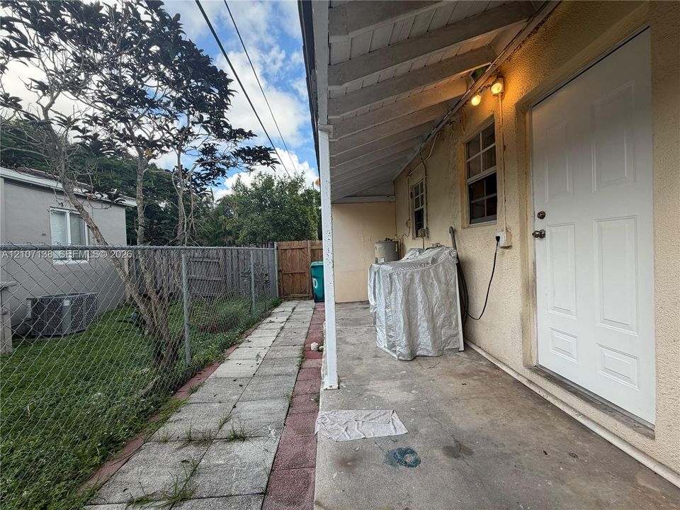 Covered concrete patio with a paneled exterior door, exposed rafter tails, and a chain-link fenced yard