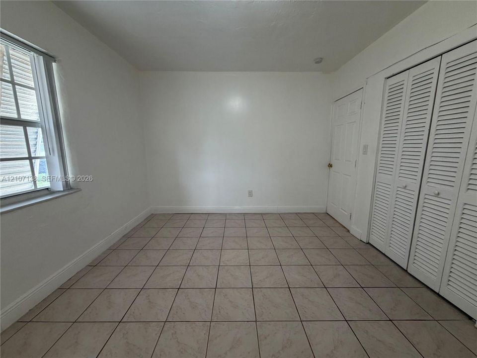 Room featuring neutral tile flooring, multi-pane window with white trim, and double louvered closet doors