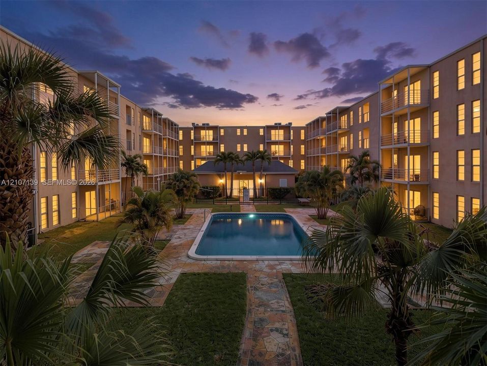 Courtyard featuring a swimming pool, stone-paver decking, grass landscaping, and multi-story buildings with tiered balconies