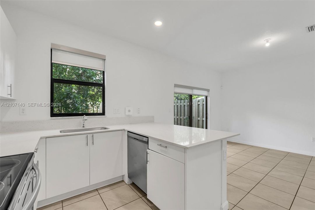 Kitchen featuring white cabinetry, solid surface countertops, stainless steel dishwasher, tile flooring, and recessed lighting