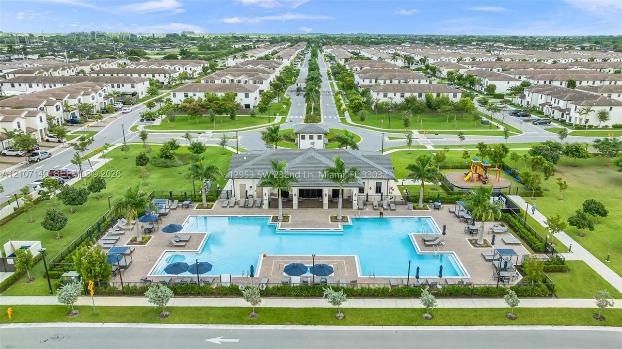 Community clubhouse featuring a large swimming pool, paved pool deck, and outdoor recreational area with playground equipment