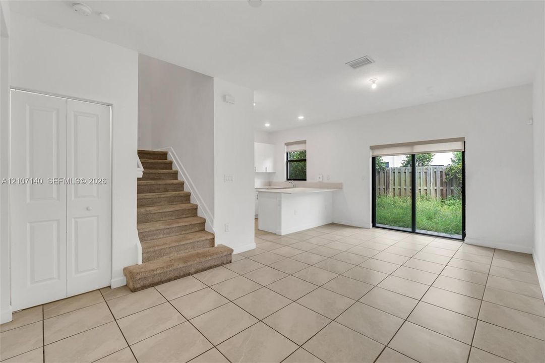 Open-concept floor plan with ceramic tile flooring, kitchen island, carpeted staircase, and sliding glass doors