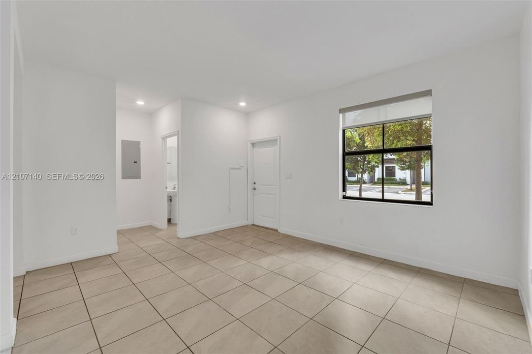 Neutral interior featuring large-format ceramic tile flooring, recessed lighting, and a single-pane window with a roller shade
