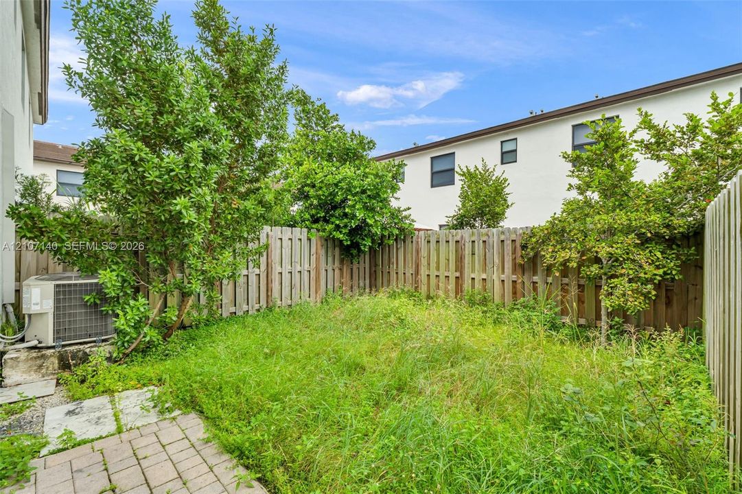 Rear outdoor space featuring a paved patio, perimeter wood fencing, and established greenery