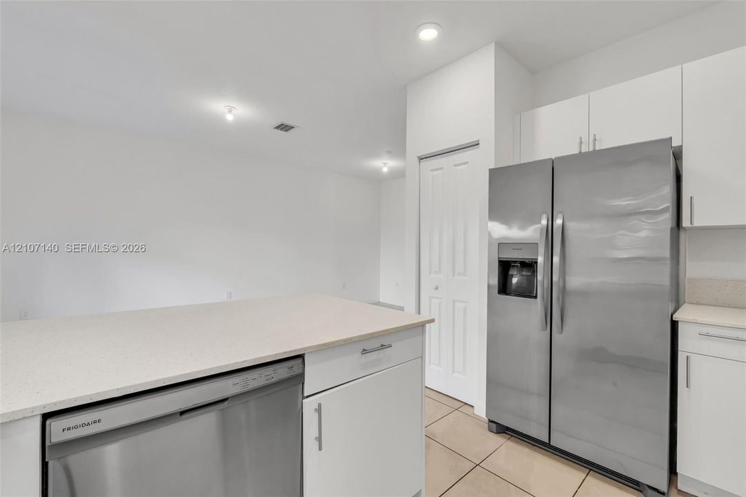 Kitchen featuring white shaker-style cabinetry, quartz countertops, stainless steel side-by-side refrigerator, stainless steel dishwasher, and tile flooring