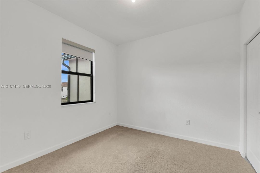Neutral-toned wall paint, plush carpeting, single-hung window with a dark frame, and a white interior door