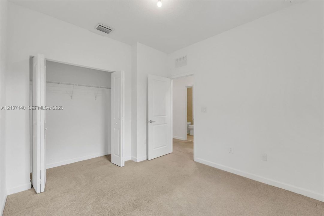 Neutral-toned interior space featuring beige carpeting, white walls, a multi-panel door, and a closet with bifold doors