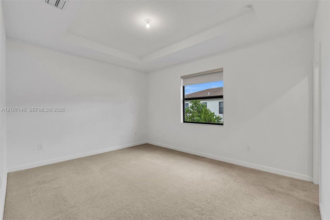 Neutral interior room featuring a tray ceiling, wall-to-wall carpeting, and a single window with a solar shade