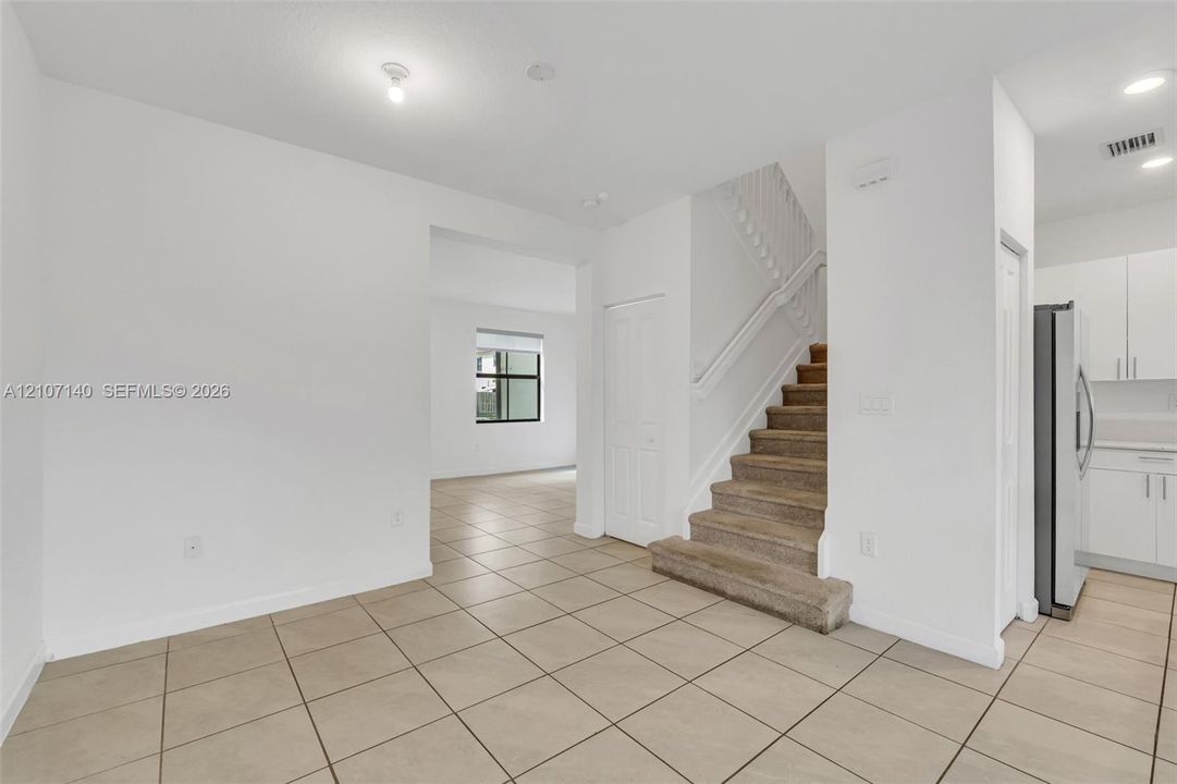 Neutral-toned tile flooring, carpeted staircase with white railings, recessed lighting, and white cabinetry