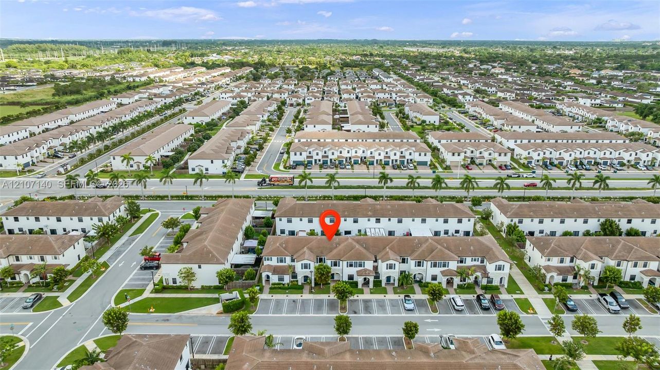 Aerial perspective of a multi-unit residential building featuring a light-toned stucco exterior, shingled roof lines, and dedicated surface parking