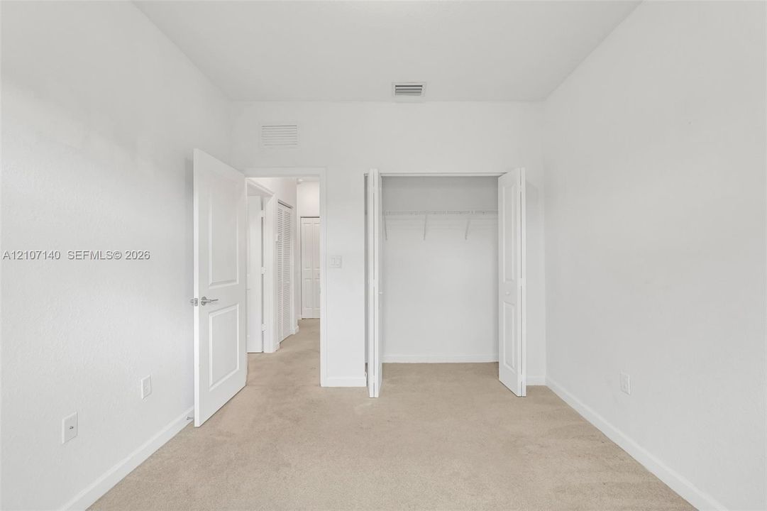 Neutral interior featuring light-toned carpeted flooring, white walls, two-panel interior doors, and a built-in closet with shelving