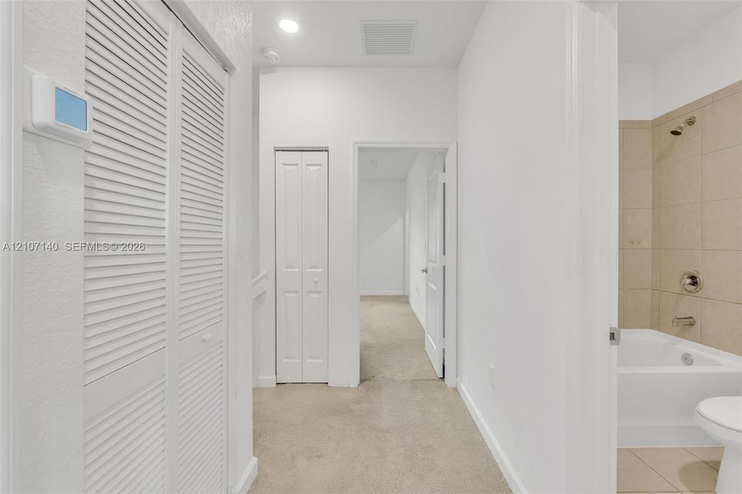 Hallway featuring dual bifold closets, neutral carpeting, recessed ceiling lighting, and a bathroom equipped with a porcelain tub, showerhead, and wall-mounted plumbing fixtures