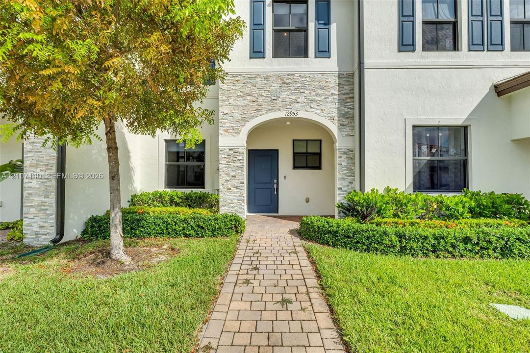 Exterior facade featuring a stone veneer entryway, arched portico, paver walkway, and dark-toned window shutters