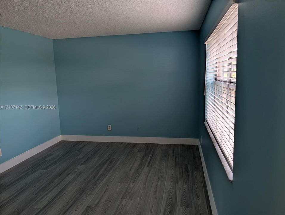 Room with wood-finish flooring, textured ceiling, and horizontal window blinds
