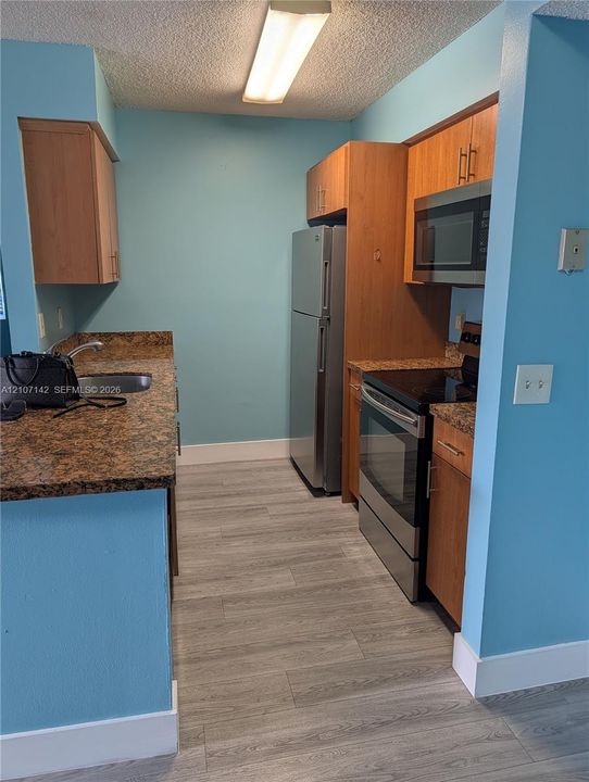Kitchen featuring wood-finish cabinetry, stone-surface countertops, stainless steel appliances, and wood-finish flooring
