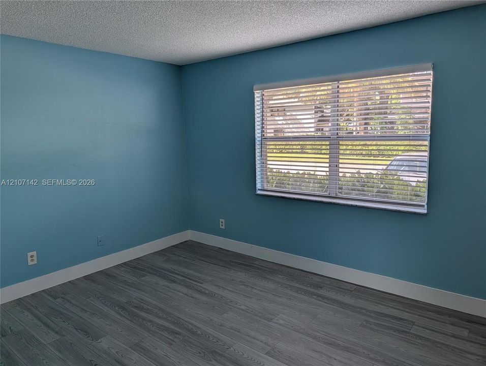 Interior space featuring wood-finish flooring, light blue wall paint, and a horizontal window with attached blinds