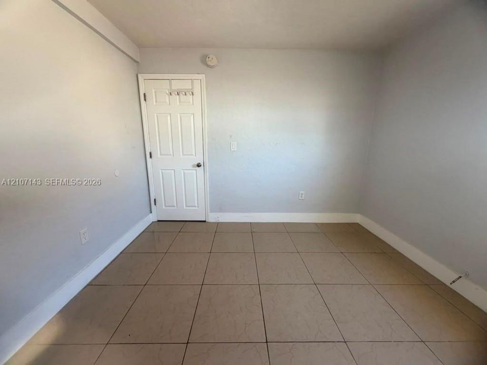 Room interior featuring large-format neutral floor tiling and a six-panel white door with brushed metallic hardware