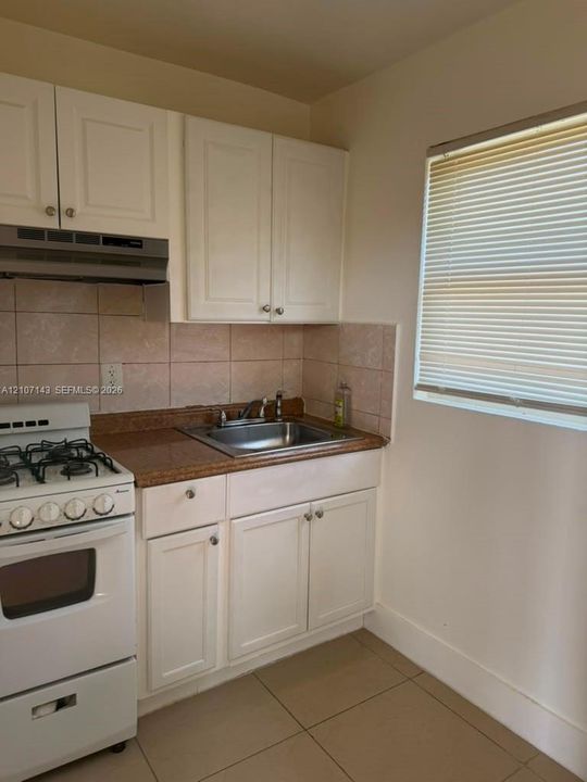 Kitchen featuring white cabinetry, solid surface countertop, stainless steel drop-in sink, tile backsplash, and tile flooring