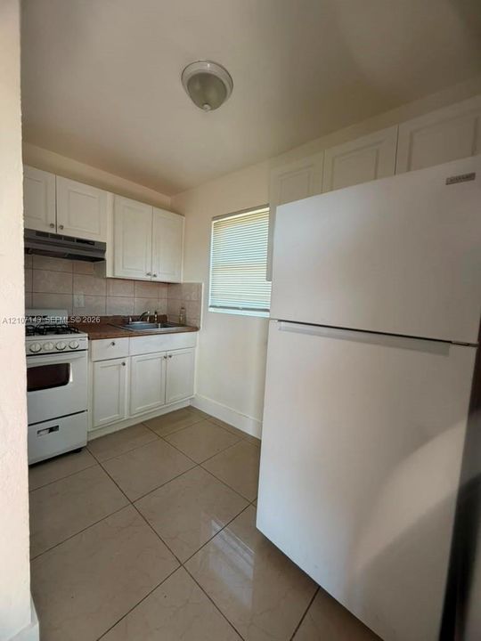 Kitchen featuring white cabinetry, tile flooring, stone-surfaced countertops, a stainless steel sink, and a tiled backsplash