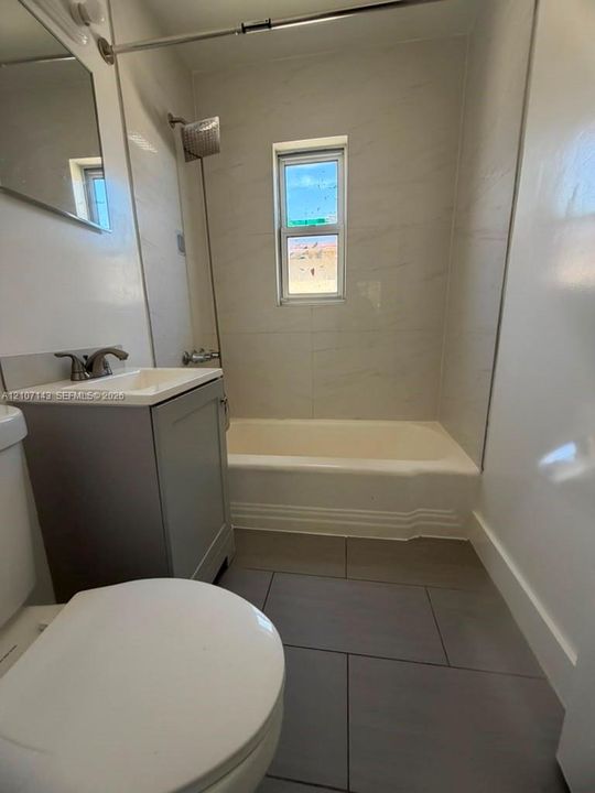 Full bathroom featuring large-format grey floor tile, white wall-surround tile, a single-basin vanity with a neutral finish, and a soaking tub