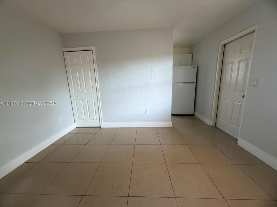Interior space featuring neutral wall paint, large-format tile flooring, two six-panel closet doors, and a built-in refrigerator
