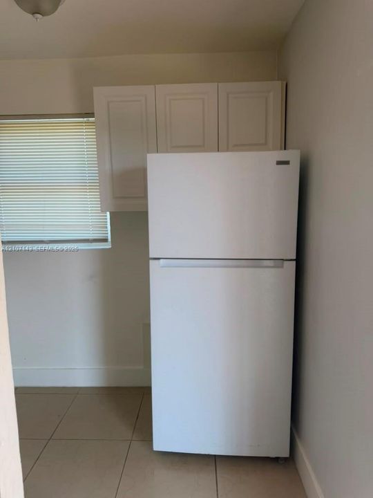 White top-freezer refrigerator, white shaker-style cabinetry, and large-format tile flooring