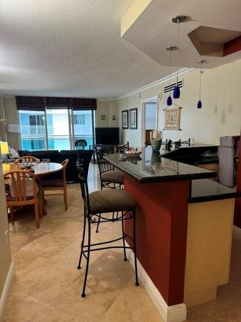 Kitchen featuring a stone-surface breakfast bar, light-tone cabinetry, and pendant lighting, complemented by tile flooring and sliding glass door access to an exterior balcony