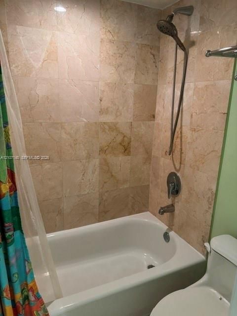Bathtub with integrated shower featuring stone-tile surround, adjustable handheld shower head, and polished metal hardware