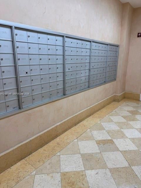Wall-mounted integrated mail distribution center with metallic finish, light-toned stone wall surfacing, and diamond-patterned stone floor tiling