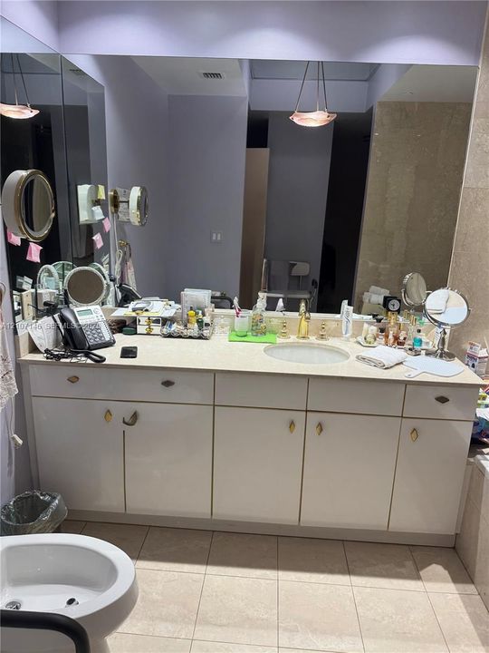 Bathroom vanity featuring a solid surface countertop, an integrated oval sink, white cabinetry with gold-tone hardware, a full-width wall mirror, and pendant lighting