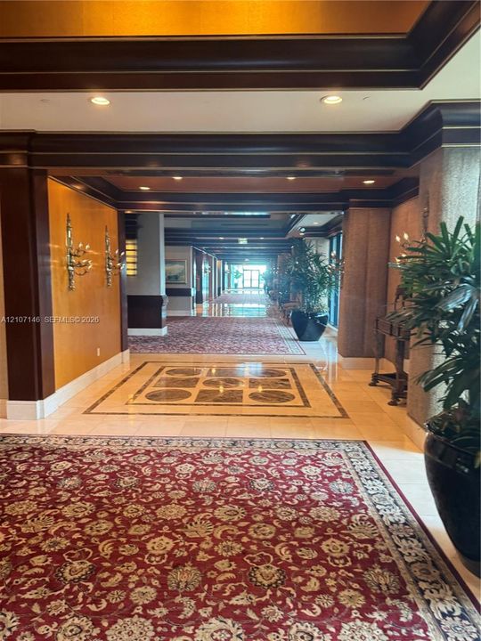 Grand corridor featuring intricate stone inlay flooring, recessed lighting, crown molding, wall sconces, and wood-finish trim details