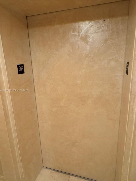 Textured Venetian plaster wall finish featuring a neutral tone, matte metal unit identification plaque, and integrated wall-mounted call button