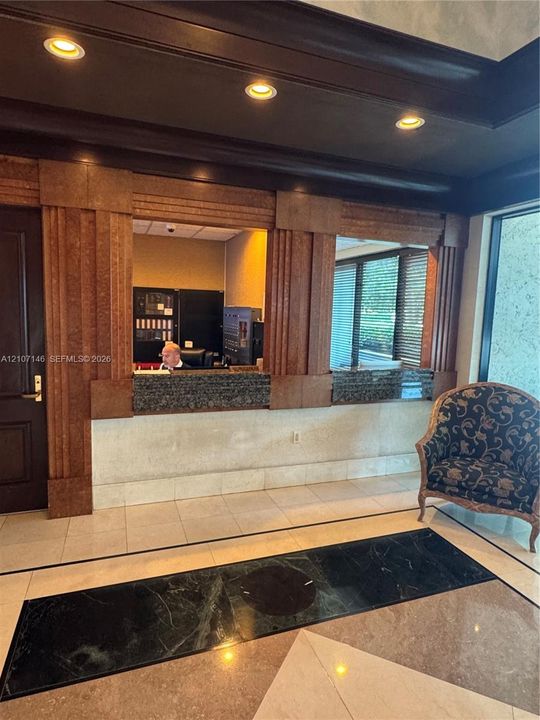 Reception area featuring a stone-topped service counter, decorative fluted wood-finish columns, recessed ceiling lighting, and polished stone tile flooring with a contrasting inlay