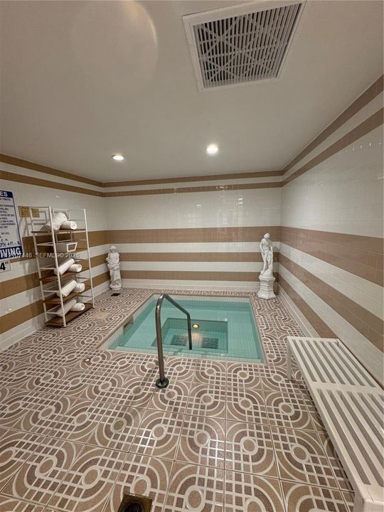In-ground jetted spa featuring decorative tile flooring, horizontally striped wall tiling, and a stainless steel grab bar