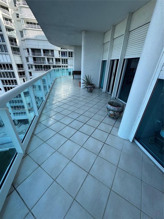 Curved balcony featuring large-format diagonal tile flooring, white structural pillars, and a glass-panel railing