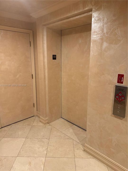 Elevator lobby featuring smooth-finish wall treatment, crown molding, and large-format tile flooring