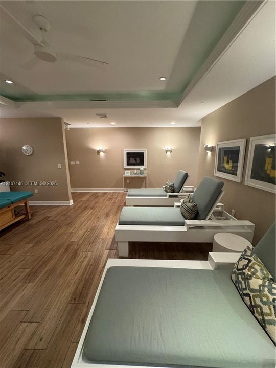 Recessed tray ceiling featuring integrated lighting, wood-finish flooring, and wall-mounted sconces