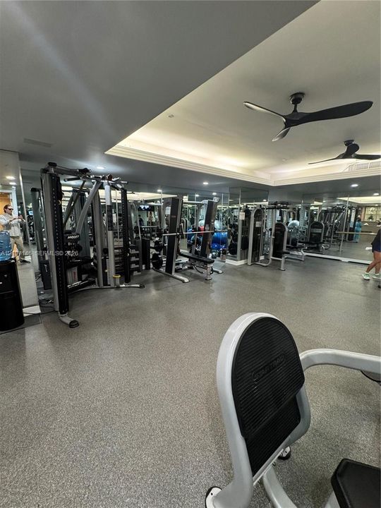 Fitness facility featuring high-impact rubber flooring, full-length wall mirrors, recessed lighting, and dual modern ceiling fans